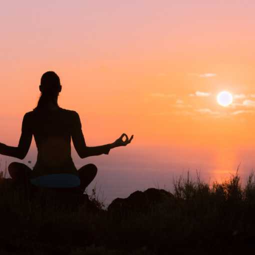 There is a women looking for some peace of mind. It looks like a yoga pose on top of a hill overlooking a sunset.